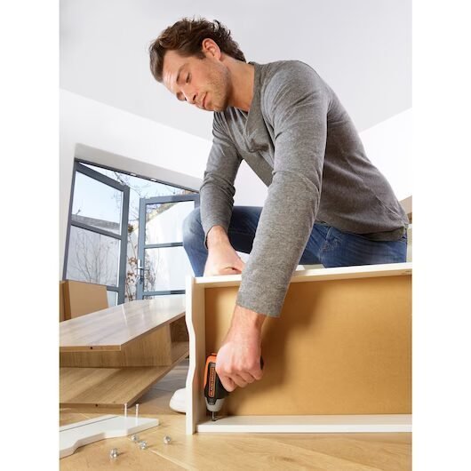 Hombre ensamblando mueble en casa con herramientas.