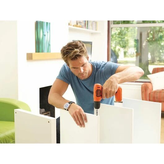 Hombre ensamblando mueble con taladro eléctrico en casa.