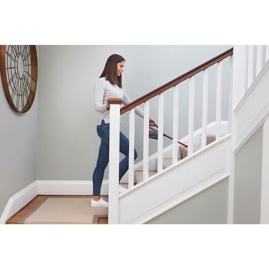 Mujer limpiando escaleras con aspiradora portátil.