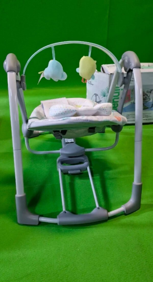 Columpio infantil con juguetes colgantes en fondo verde.