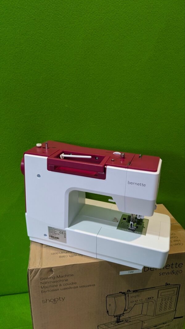 Máquina de coser sobre caja, fondo verde.