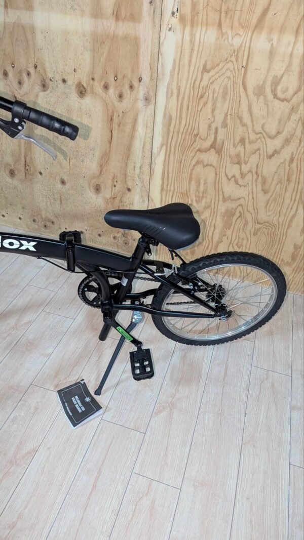 Bicicleta plegable negra junto a pared de madera.