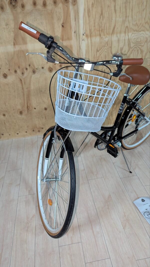 Bicicleta negra con cesta blanca en suelo de madera.