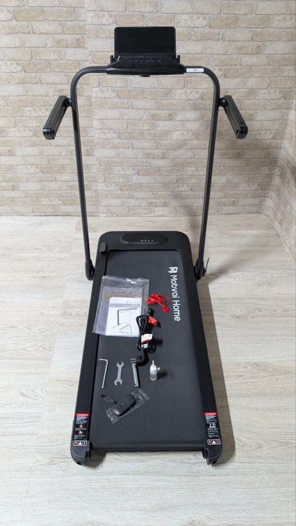 Cinta de correr plegable con accesorios sobre superficie gris.