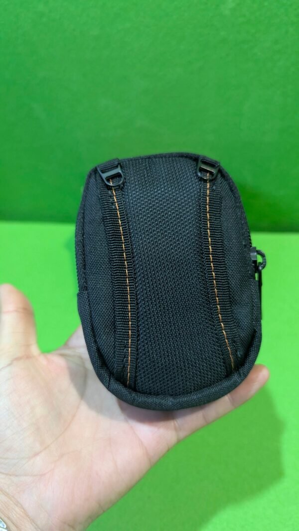 Pequeño estuche negro en mano sobre fondo verde.