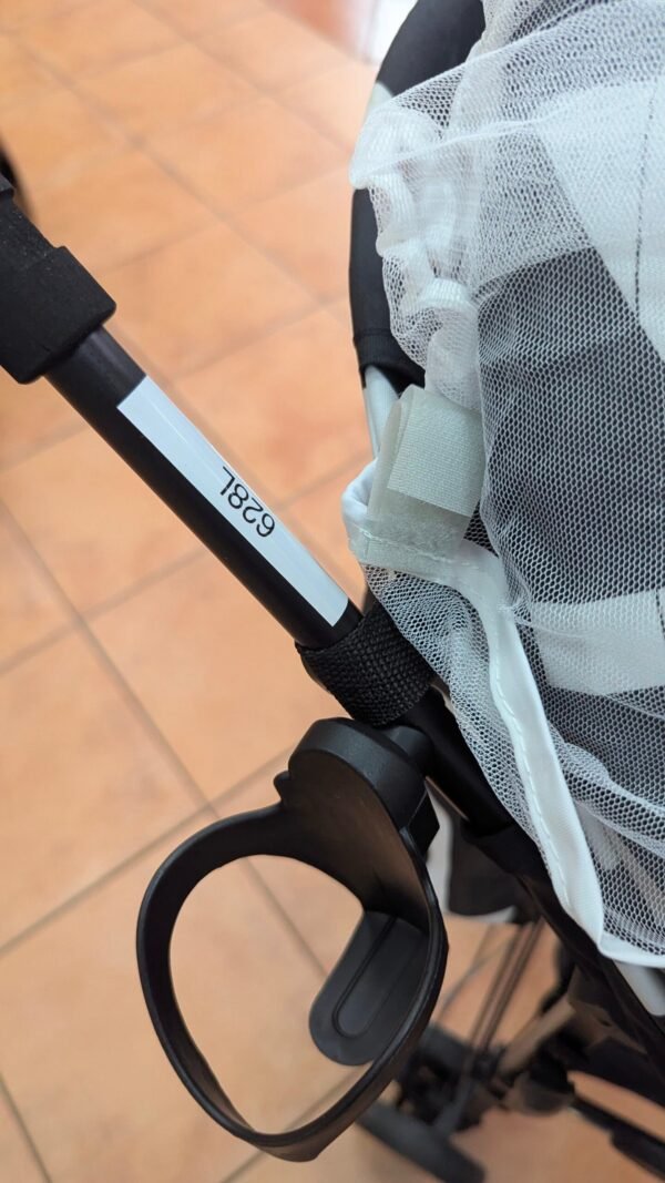Detalle cochecito de bebé con soporte y red blanca.