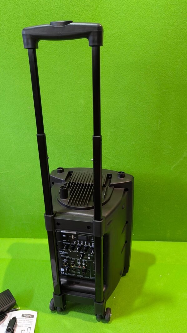 Altavoz con ruedas y asa retráctil en fondo verde.