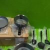 Juego de sartenes y utensilios sobre caja, fondo verde.