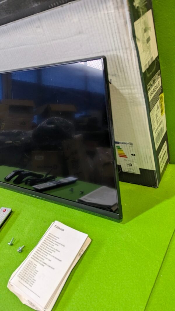 Televisor con control remoto y manual en mesa verde.