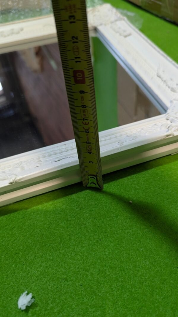 PXL_20251113_120340446-scaled-1.jpg Cinta métrica midiendo marco blanco sobre césped verde.