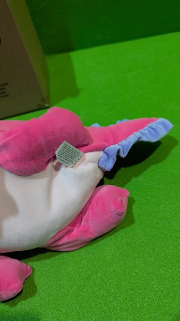 Peluche rosa con cola azul en el suelo.