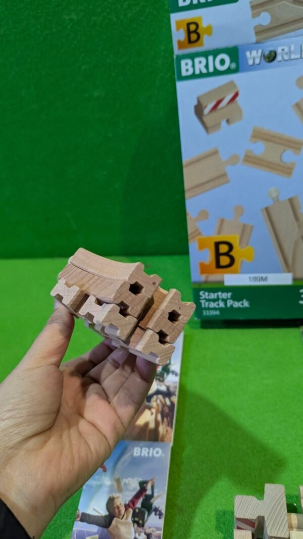 PXL_20251120_120329200.MP_-scaled-1.jpg Mano sosteniendo piezas de vía de tren de madera.