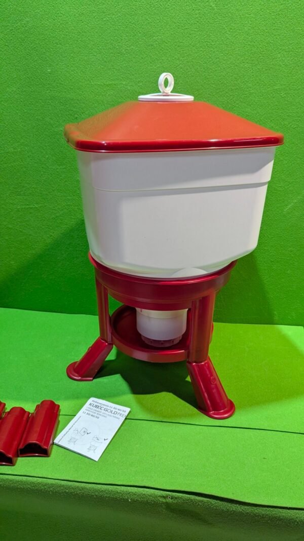 Bebedero rojo y blanco para animales sobre fondo verde.