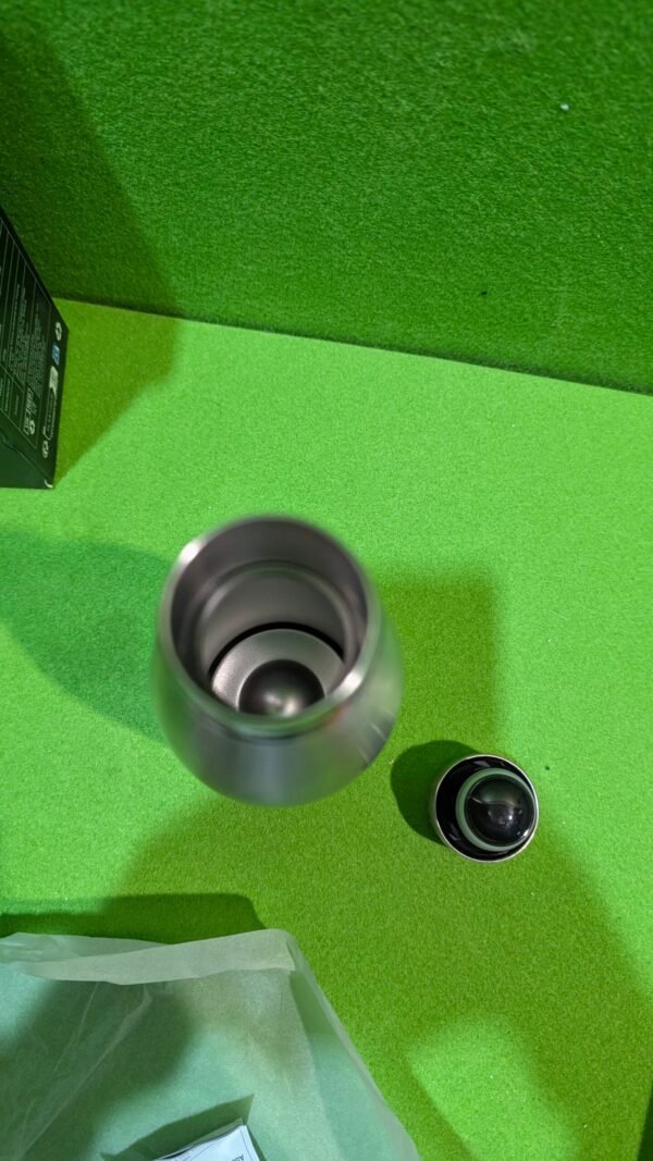 PXL_20260106_192805189-scaled-1.jpg Tapa y botella de acero inoxidable sobre mesa verde.