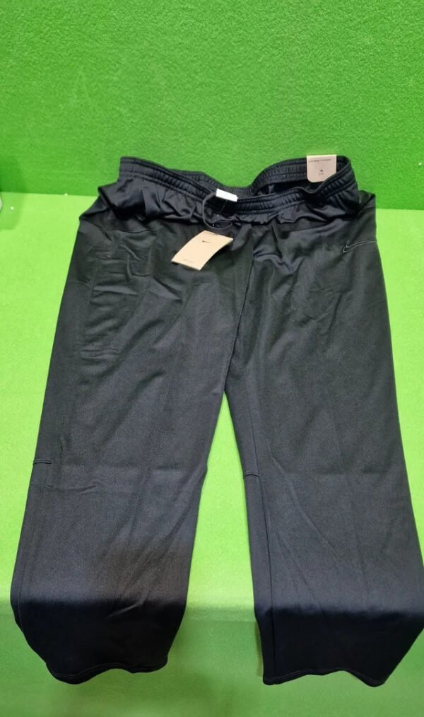 Pantalones deportivos negros con etiquetas sobre césped verde.