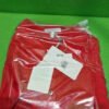 Camisa roja empaquetada en bolsa transparente sobre fondo verde.