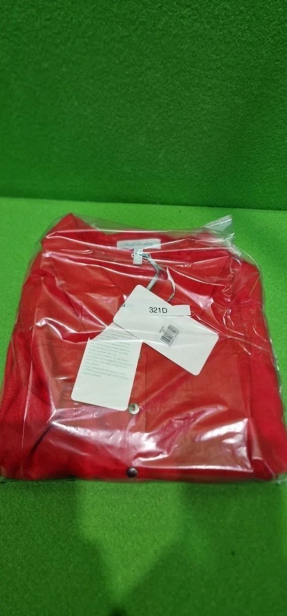 Camisa roja empaquetada en bolsa transparente sobre fondo verde.