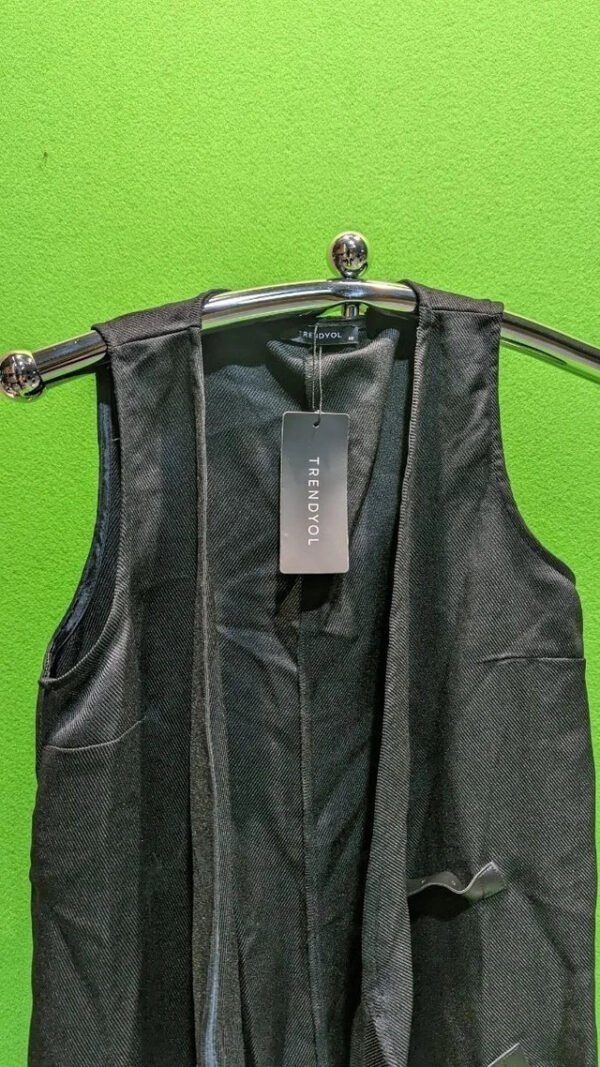 Chaleco negro con etiqueta en percha verde brillante.