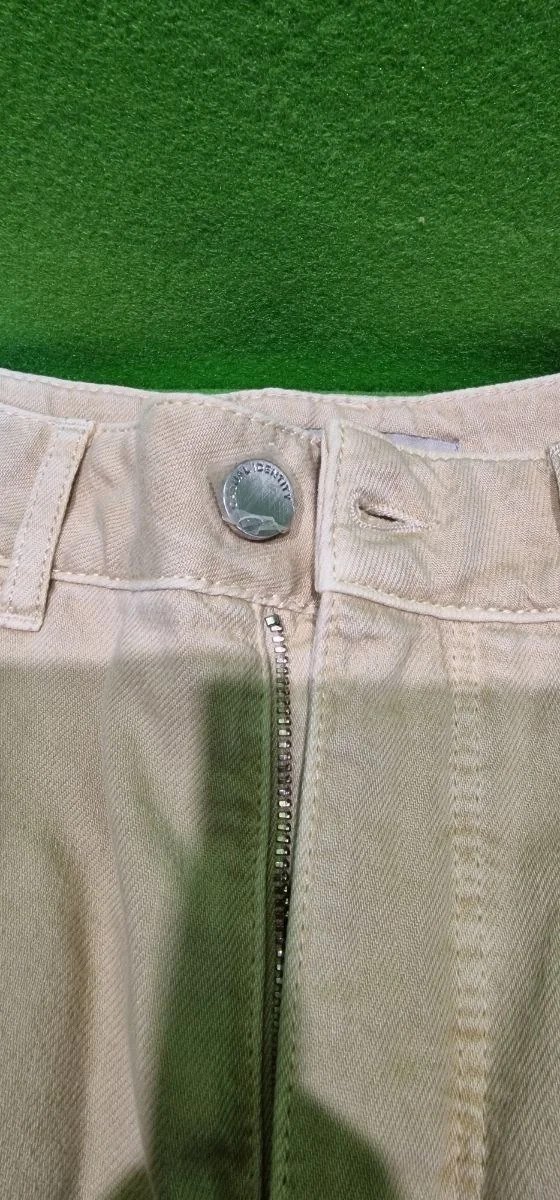 Vaqueros beige con cremallera metálica y botón plateado.