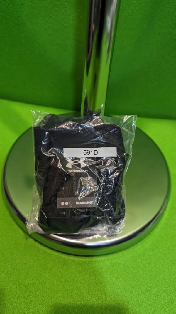 Pulsera deportiva negra en embalaje sobre superficie verde.